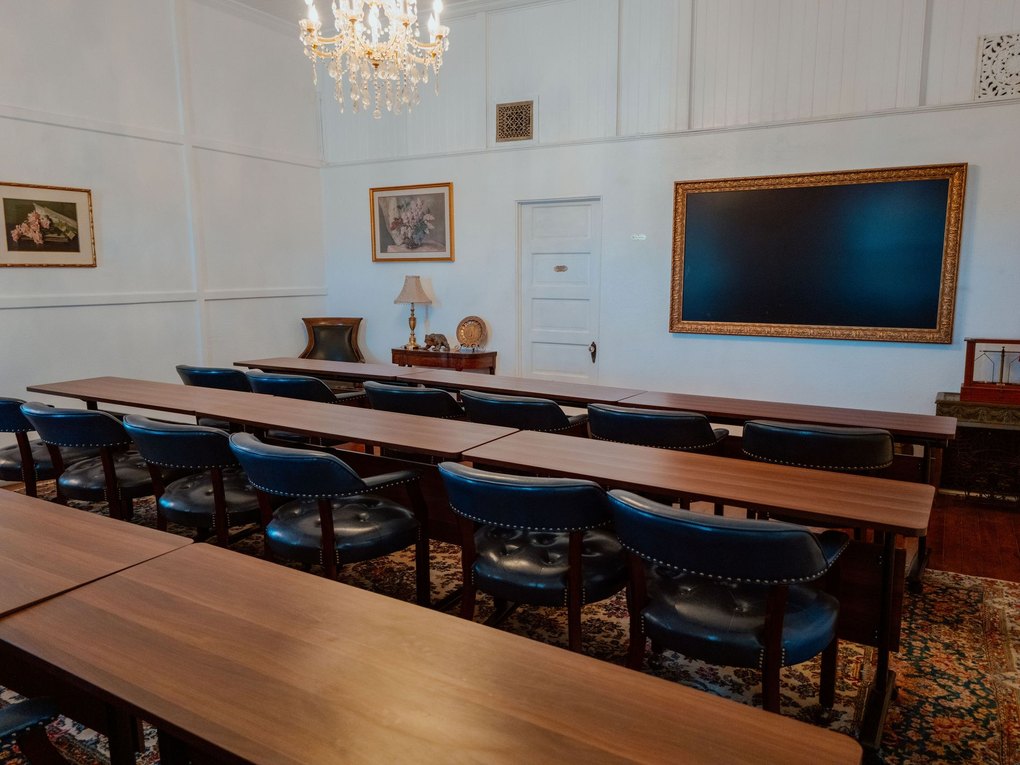 The Training Center set classroom style, with long tables and leather chairs beneath a crystal chandelier