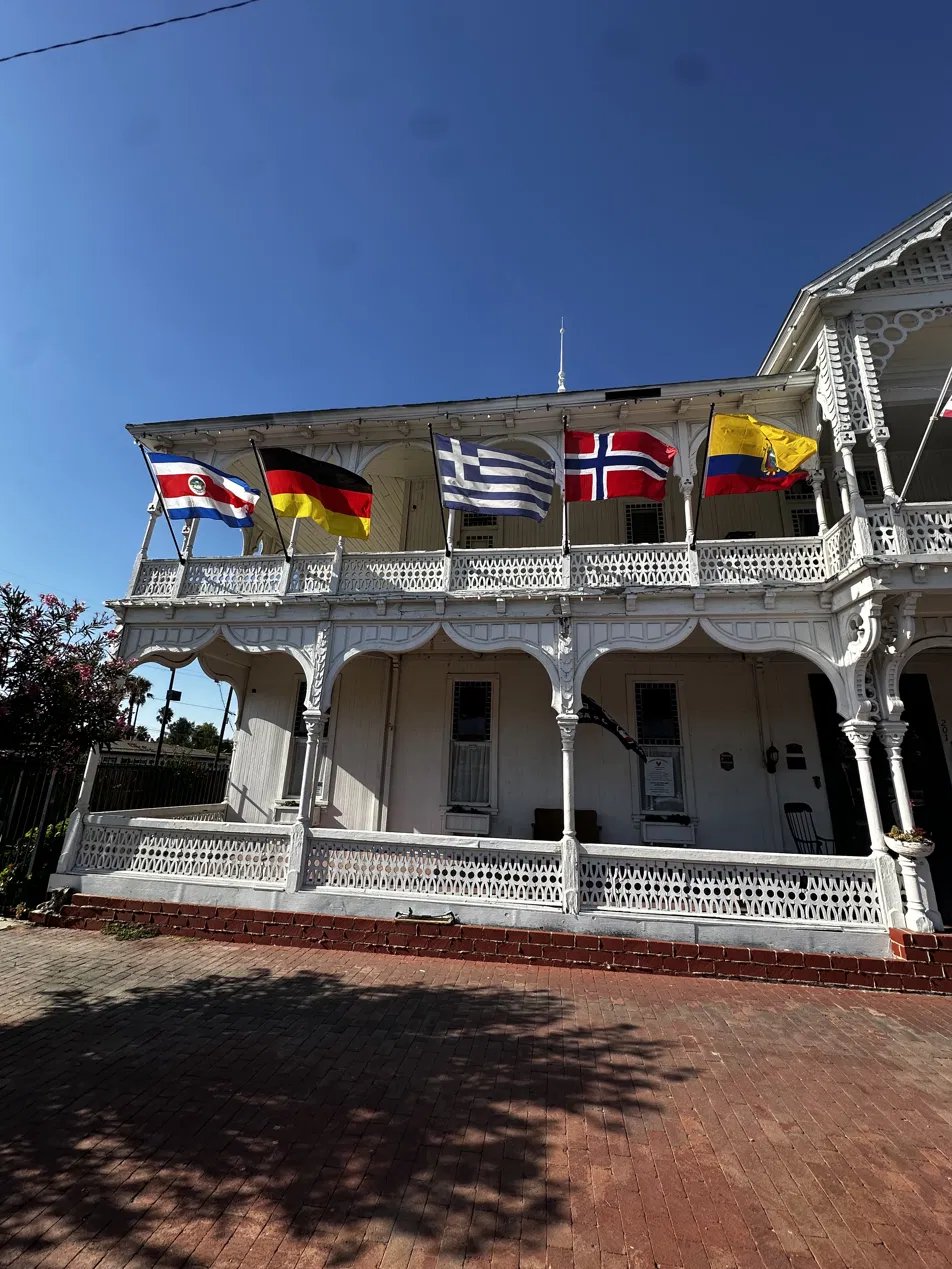 The two-story Victorian facade of the Crescent Bath House with white gingerbread trim and flags along the balcony