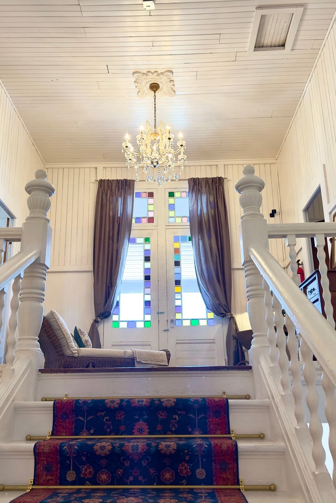 The staircase landing at The Crescent House, with a crystal chandelier above stained glass doors and a patterned stair runner