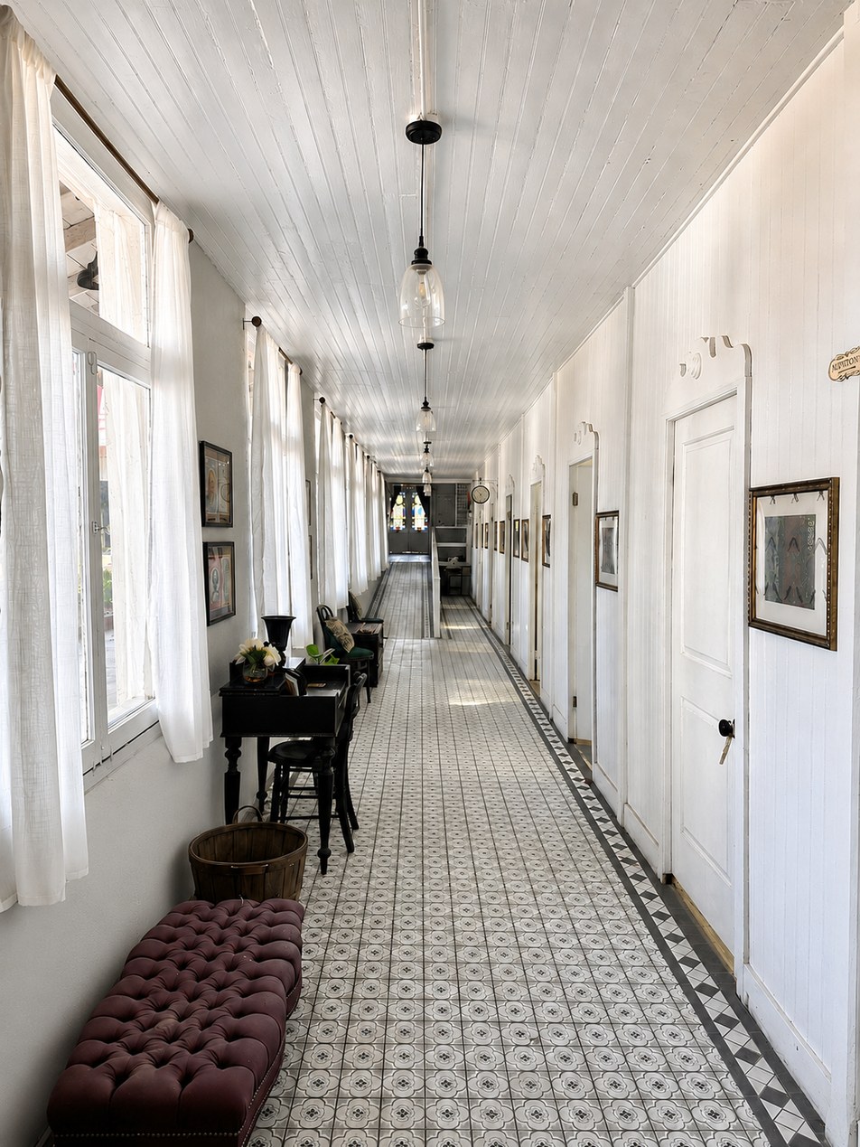 Long light-filled hallway with a patterned tile floor, pendant lights, framed prints, and stained glass at the far end