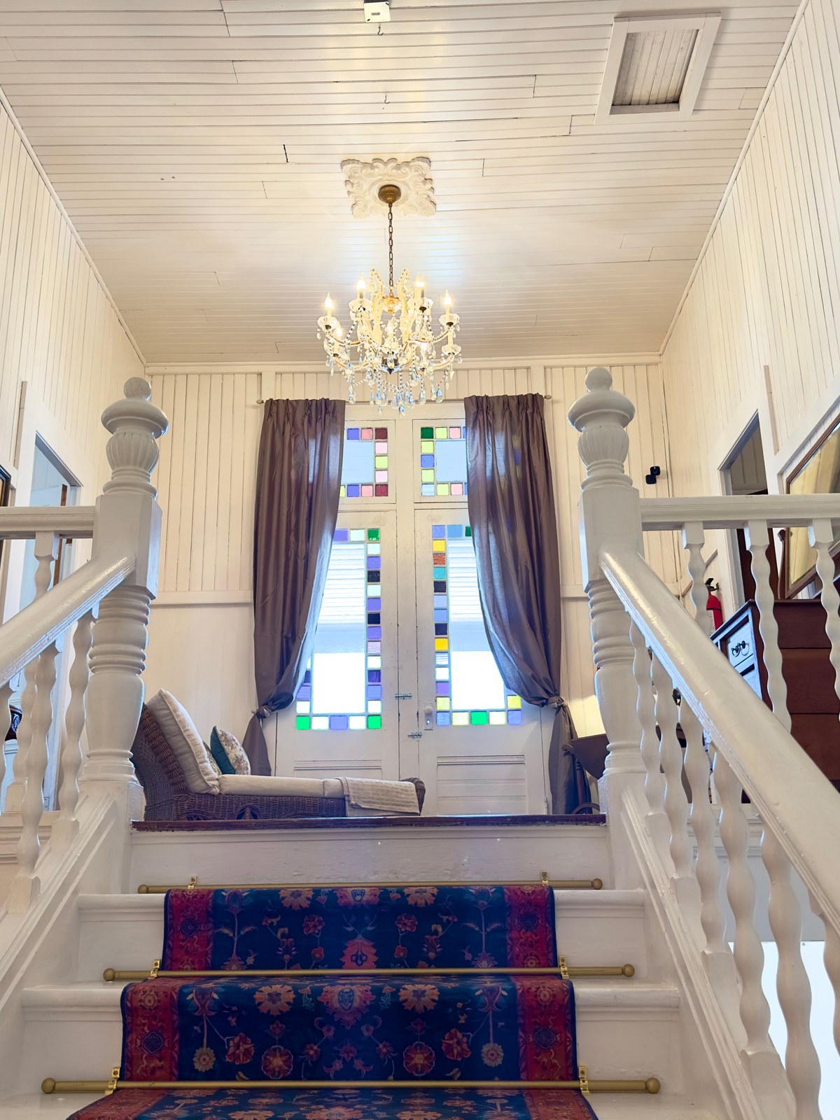 The grand interior staircase of The Crescent House, with a carved white balustrade, patterned runner, and crystal chandelier