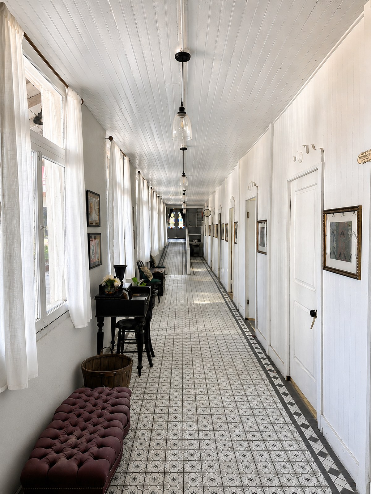 A long interior hallway at The Crescent House paved in patterned encaustic tile, lined with white doors and framed pictures