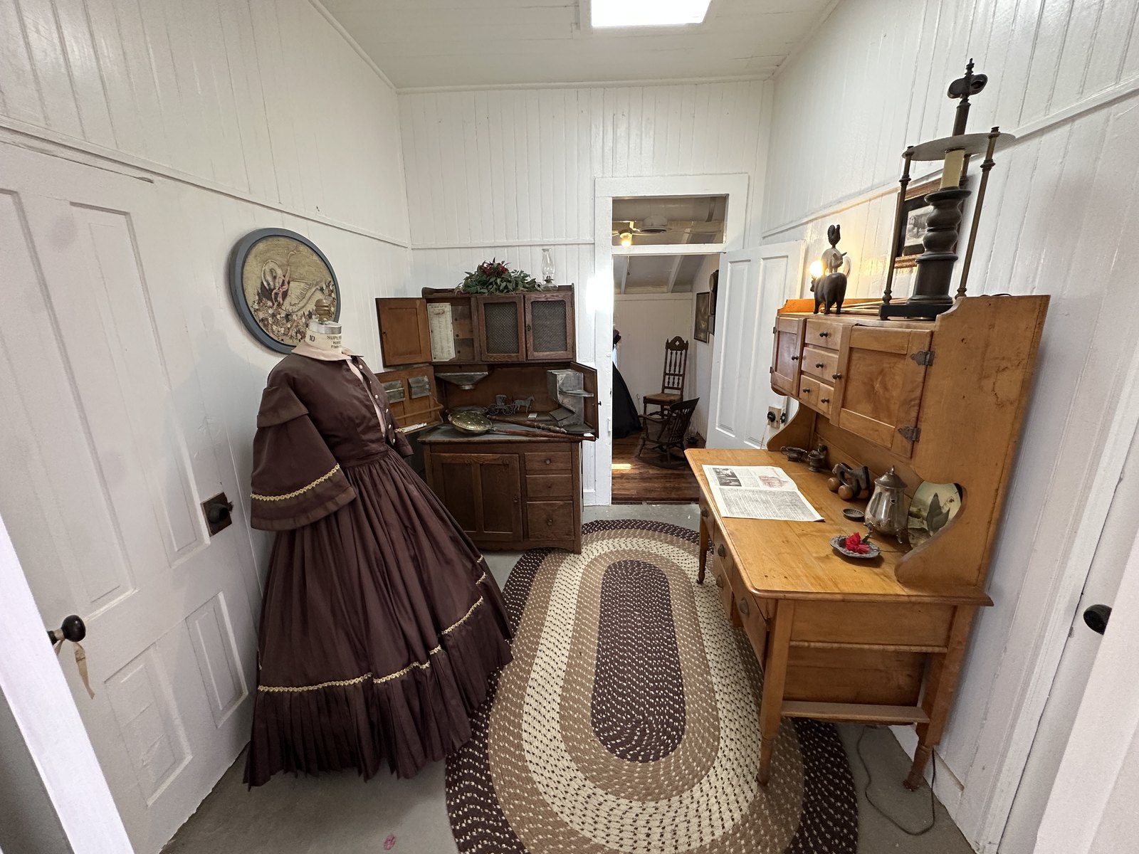 A period display room with a Victorian dress and an antique kitchen cabinet