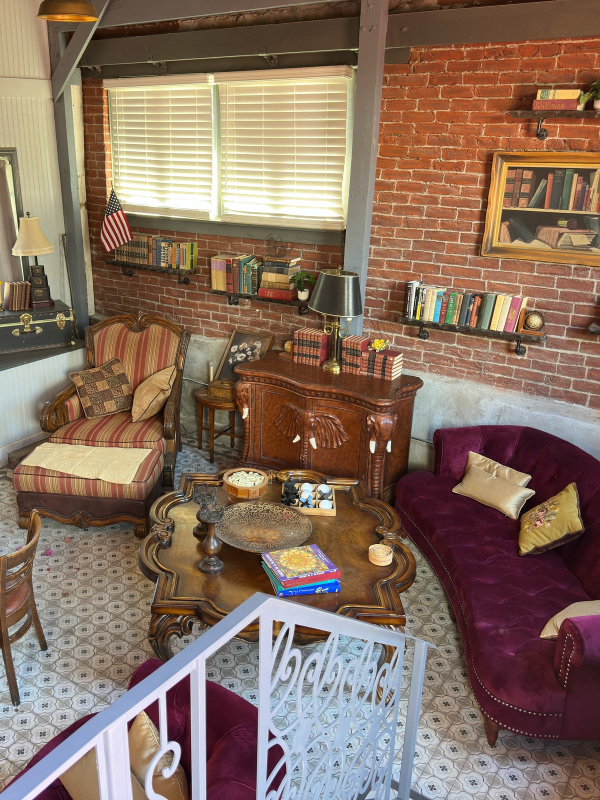 The Library Speakeasy, its brick wall lined with books beside a painted bookshelf panel, with a deep velvet sofa on the original tile