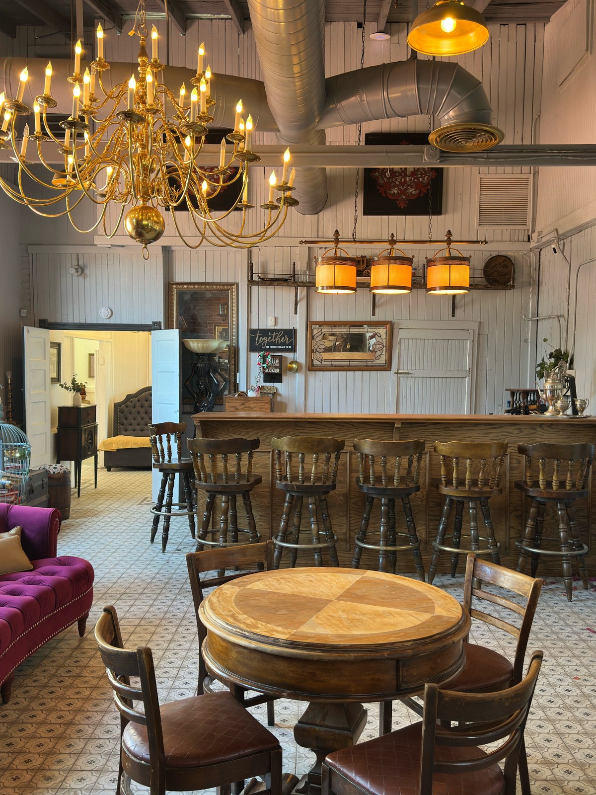A wide view of The Library Speakeasy taking in the bar, the wooden stools, the gold chandelier, and the original tile floor in one frame