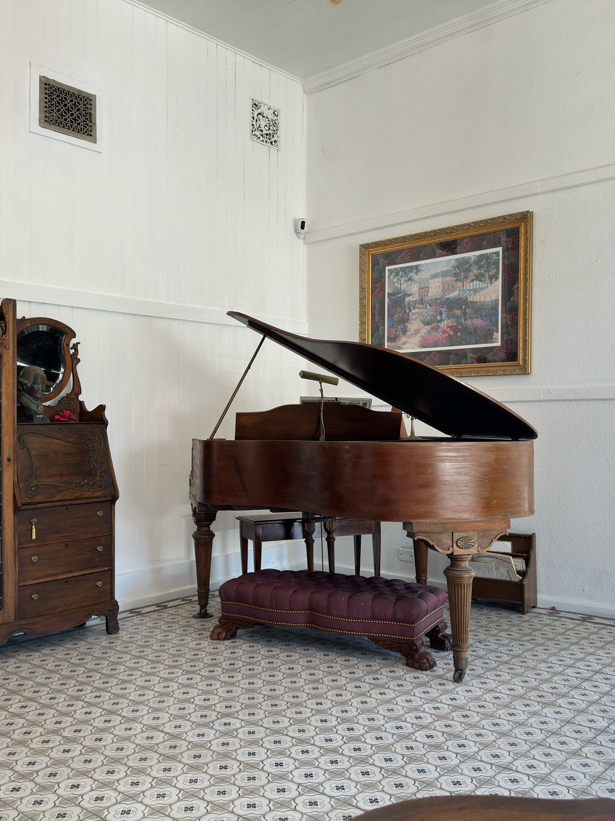 The antique grand piano beside a leaded glass secretary, on the patterned tile floor