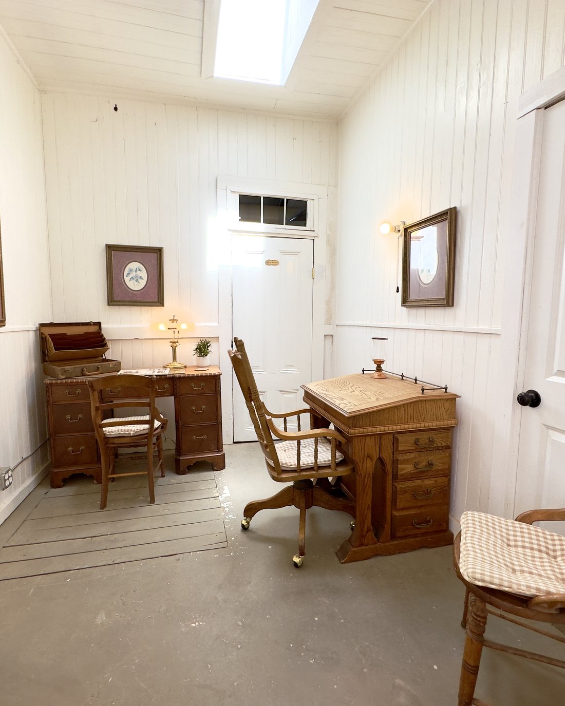 A private work room, with a writing desk beneath the skylight, a slant top desk, and original beadboard walls