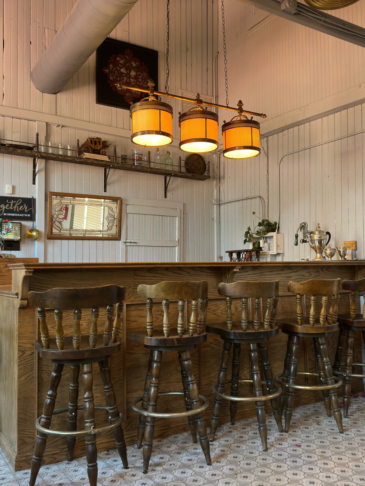 The bar inside The Library Speakeasy, with wooden stools and brass shaded lamps above the counter