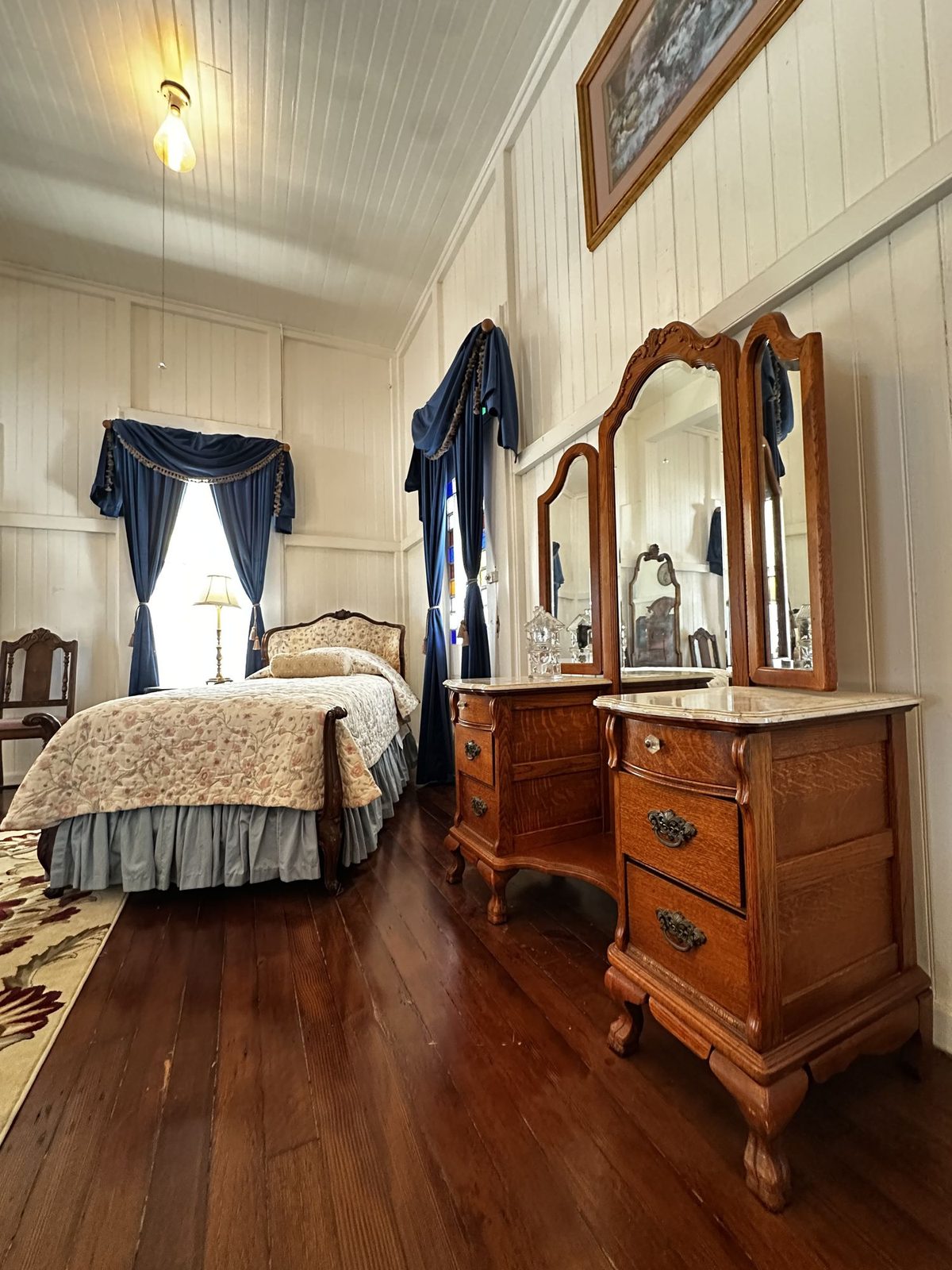 A guest room with blue drapes and a marble topped oak vanity