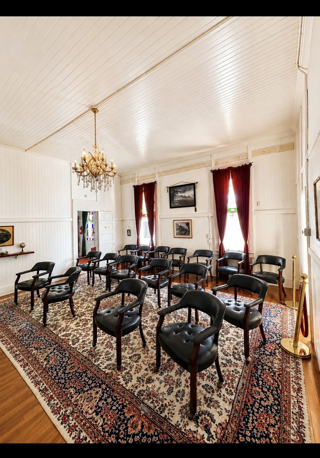 The Crescent Training Center set in rows, black leather chairs on a patterned rug beneath a brass chandelier and stained glass