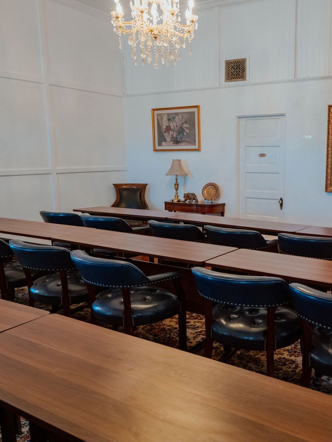 The Crescent Training Center set classroom style, long tables and blue leather chairs beneath a crystal chandelier