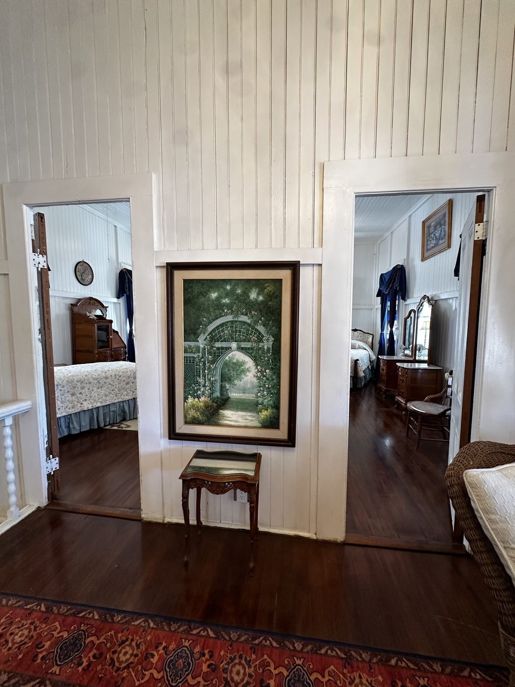 The upstairs landing, with the original red wood floors, white beadboard walls, and a framed garden painting between two bedroom doorways