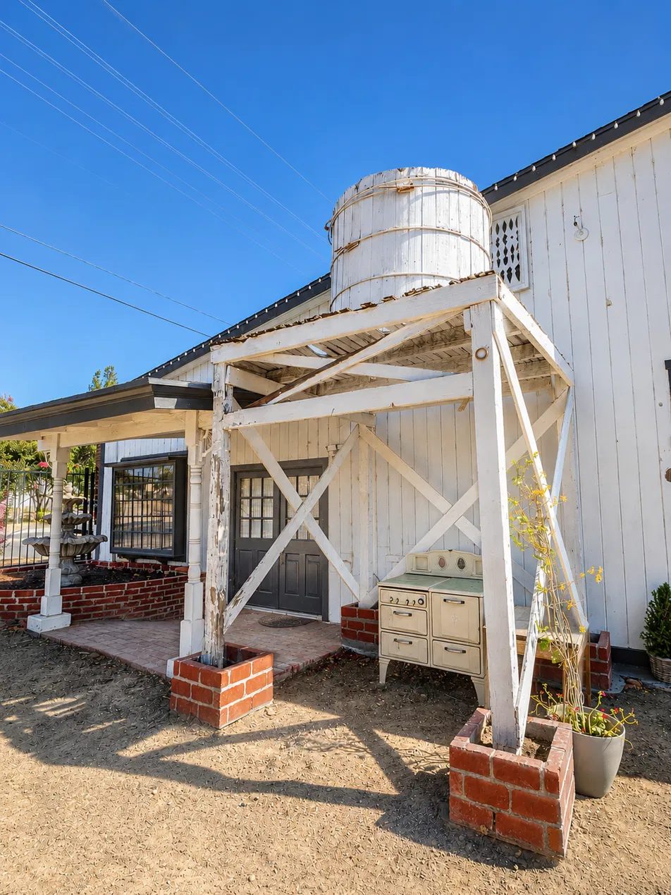 Whitewashed farmhouse corner with an original wooden water tower on a timber frame and an antique enamel stove below